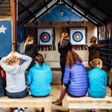 Archery   group on benches watching 2 girls fire